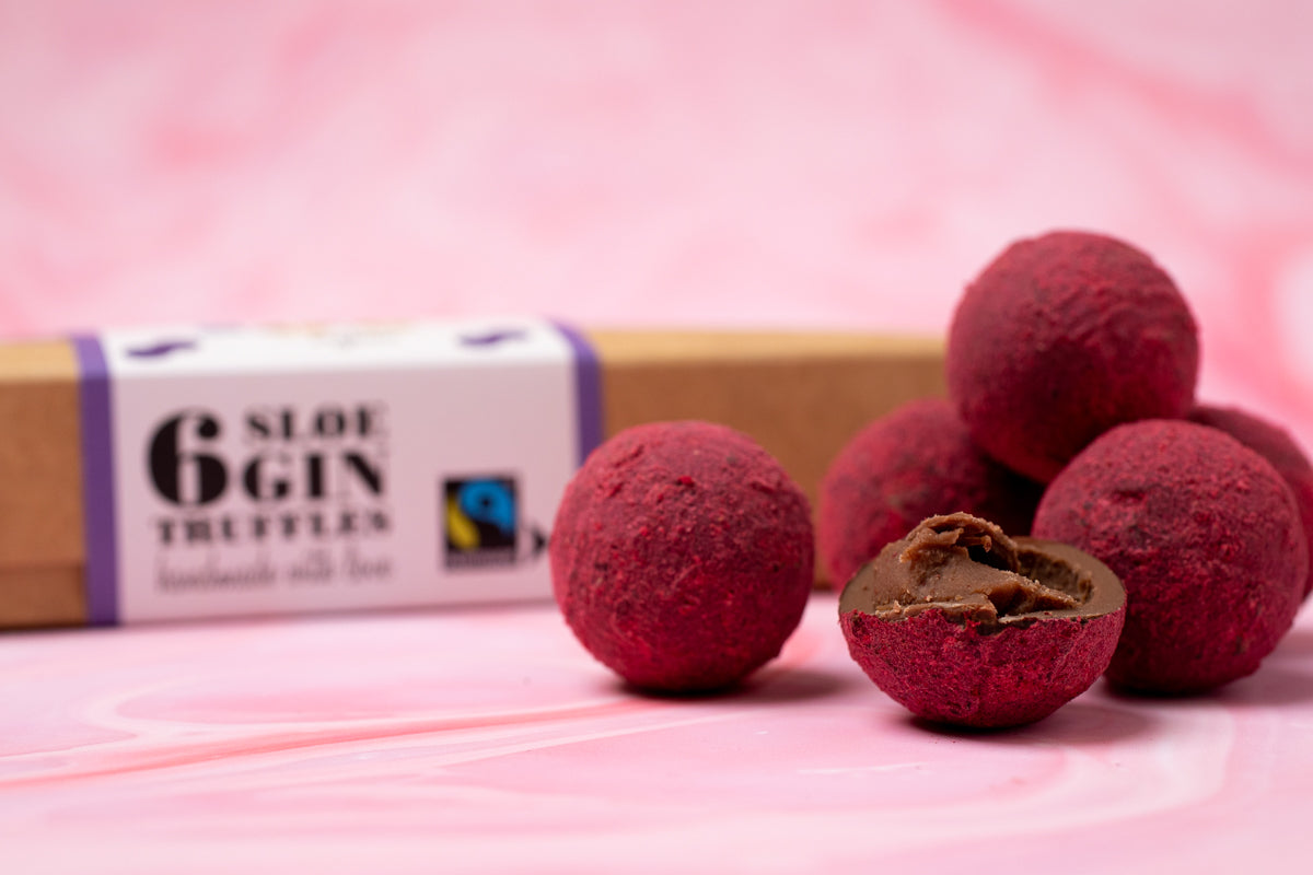 Sloe gin truffles in front of their box on a pink marble background